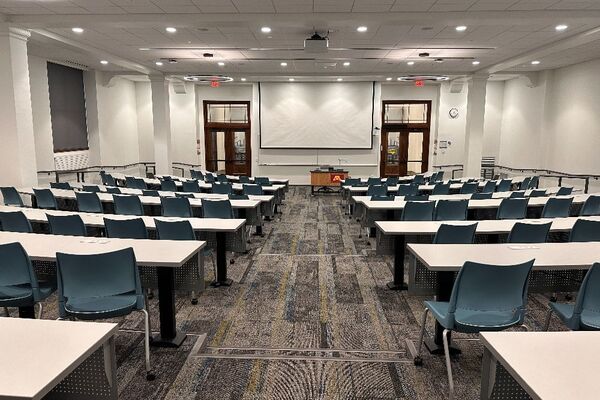 Front of room view with projection board lowered, lectern in front of markerboard, and exit doors to left and right