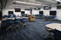 View of room showing student group seating and exit door at rear right