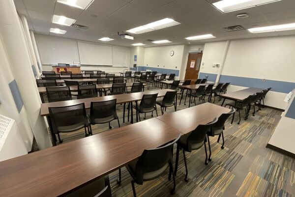 Front of room view with lectern on left in front of markerboard and projection screen lowered