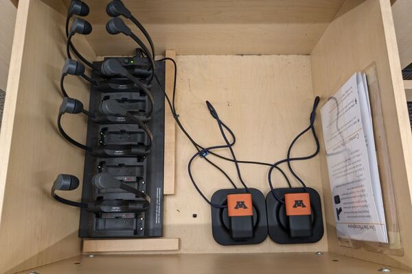 Pedestal - inside view of drawer showing two wireless mics in charging base, and assistive listening devices in charger