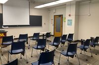 Front of room view with lectern on left in front of chalkboard and projection screen partially lowered