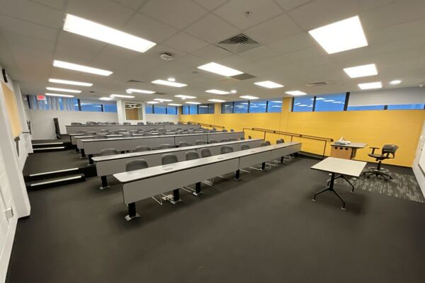 Back of room view of student fixed-table and chair seating and exit door at left rear of room