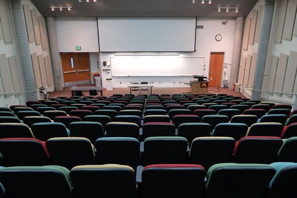 Front of room view with lectern on right in front of markerboard and projection screen lowered, double exit doors at front left of room