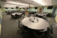 Room view with lectern in center, markerboards on all walls, exit door center left wall, and projection screen on right wall