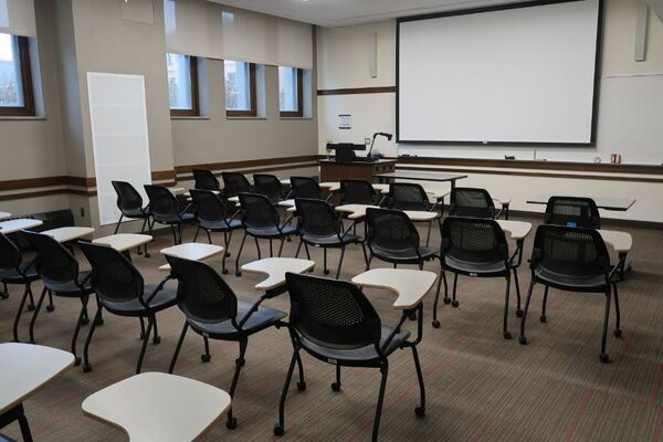 Front of room view with lectern on left in front of markerboard and projection screen partially lowered