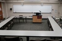 Front of room view with lectern center in front of markerboard, exit door on  left wall near front of room