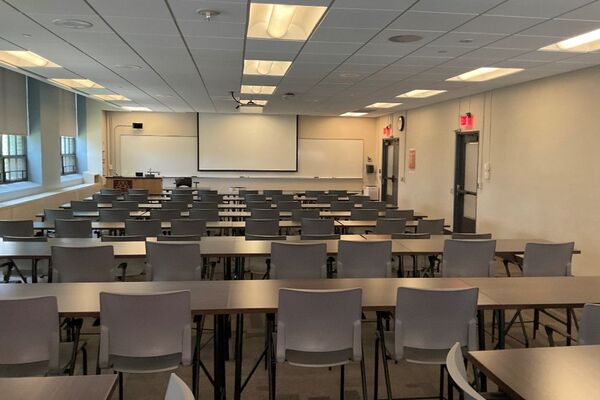 Front of room view with lectern on left in front of markerboard and projection screen lowered