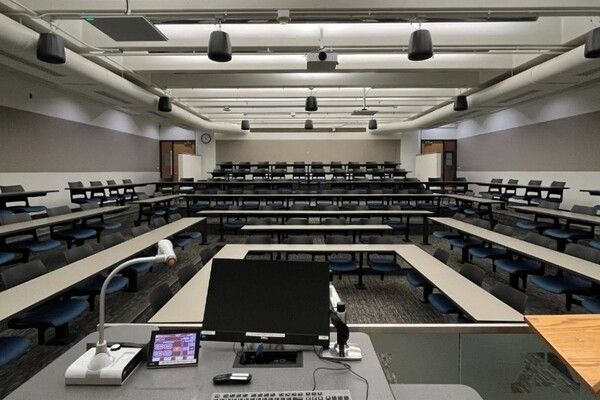 Back of room view of student fixed table and chair seating and exit doors at rear of room