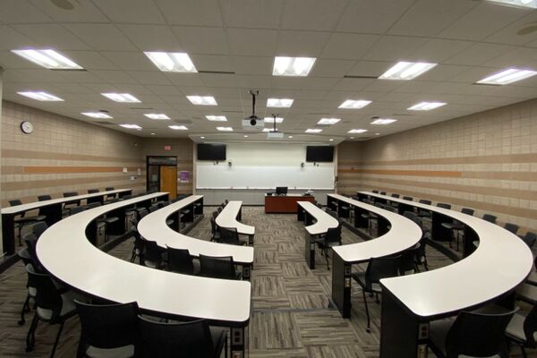 Front of room view with lectern on center in front of markerboard and display screens to left and right, exit door on the left