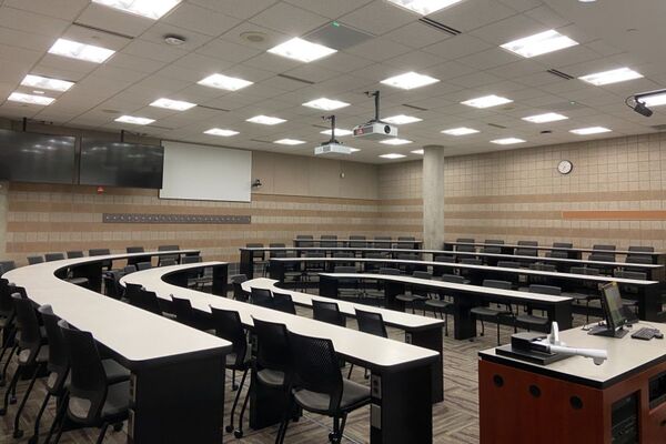 Back of room view of student tiered fixed-table and chair seating and  exit door at rear of room