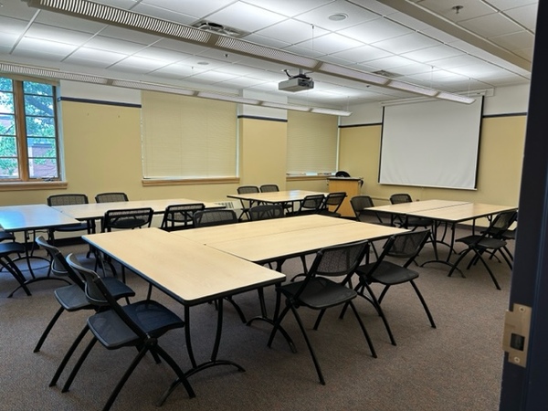 Photo of front of room from back of room with windows on the left.  Tables set in 2 groups of 4 and 2 groups of 6.