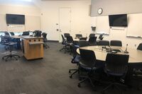 View of lectern, student collaborative table and chair seating, monitors and markerboards on all walls