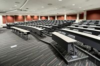 Back of room view of student tiered fixed table and chair seating and double exit door at right rear of room