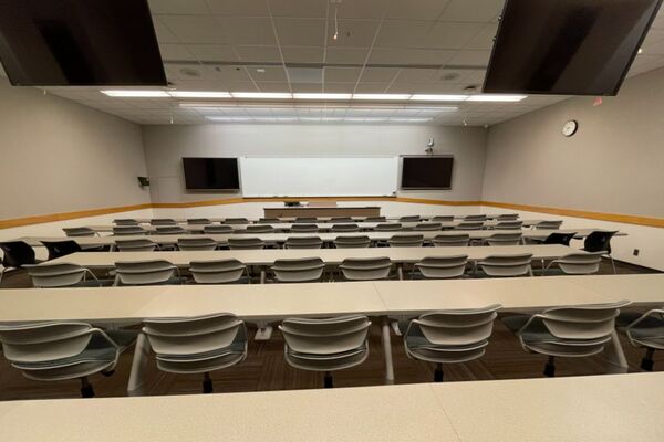 Front of room view with lectern center in front of markerboard and display screens to left and right