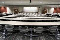 Front of room view with lectern on right in front of markerboard, exit doors on left and right of markerboard