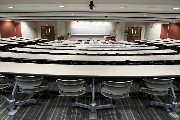 Front of room view with lectern on right in front of markerboard, exit doors on left and right of markerboard