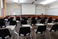 Front of room view with lectern on left in front of markerboard and projection screen lowered