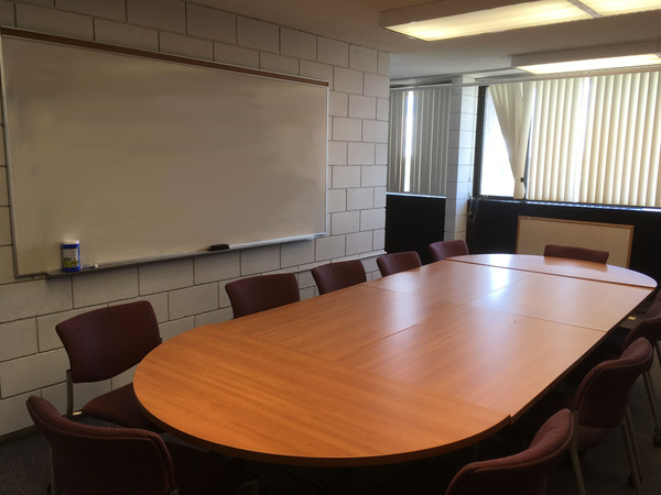 Photo of front of room from back of room, window on wall and conference room table seating.