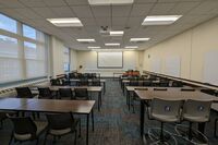 Front of room view with lectern on right in front of markerboard, screen lowered