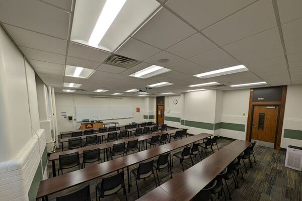 Front of room view with lectern on left in front of markerboard and exit door on the right