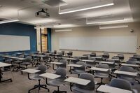 Back of room view of student tablet arm seating and markerboards on side and rear walls, exit door at rear left of room