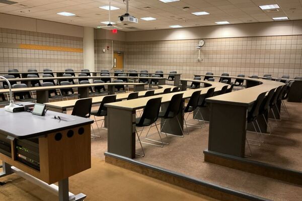 Back of room view of student tiered fixed-table and chair seating, exit door on left