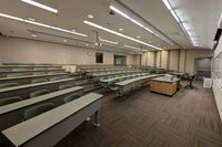 Back of room view of student tiered fixed-table and chair seating and double exit doors at right rear of room