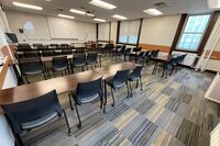 Front of room view with lectern on right in front of markerboard, projection screen lowered