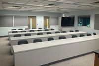 Back of room view of student table and chair seating and confidence monitor at right rear of room