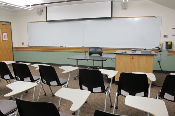 Front of room view with lectern on right in front of markerboard and projection screen partially raised