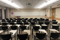 Front of room view with lectern on left in front of markerboard, and exit door on right wall