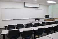 Front of room view with lectern on right in front of markerboard and projection screen partially raised