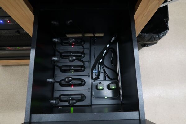 Pedestal - inside view of drawer showing two wireless mics in charging base and assistive listening devices in charger