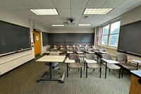 Rear of room view of student tablet arm chair seating and chalkboard in rear of room and right side of room