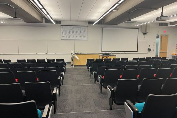 Front of room view with lectern on right side of demonstration bench in front of markerboard, exit door on right side of front wall