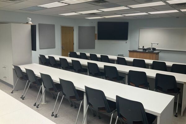 Front of room view with lectern center in front of markerboard, display monitor right, and exit door front right