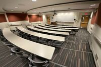 Front of room view with lectern on left in front of markerboard and exit doors on left and right of markerboard