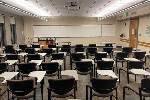 Front of room view with lectern on left in front of markerboard, exit door on right wall of room