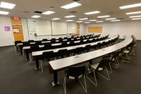 Front of room view with lectern on right in front of markerboard and projection screen lowered, exit doors to left and right