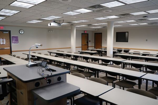 Back of room view of student table and chair seating and exit doors on left side wall