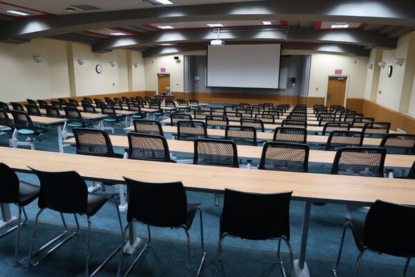 Front of room view with lectern on left in front of markerboard and projection screen lowered