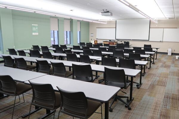 Front of room view with lectern on left in front of markerboard and projection screen lowered