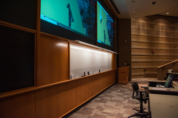 Instructor view from front right of room looking towards whiteboard/projectors.  Illuminated whiteboard, projector display, and front podium are visible.