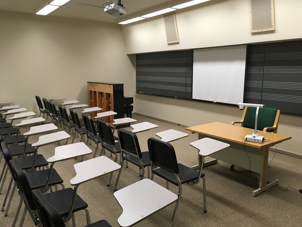 Photo of front of room from back of room with music staff chalkboard and piano.