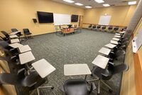 Front of room view with lectern in front of markerboard and display monitors on the left and right 