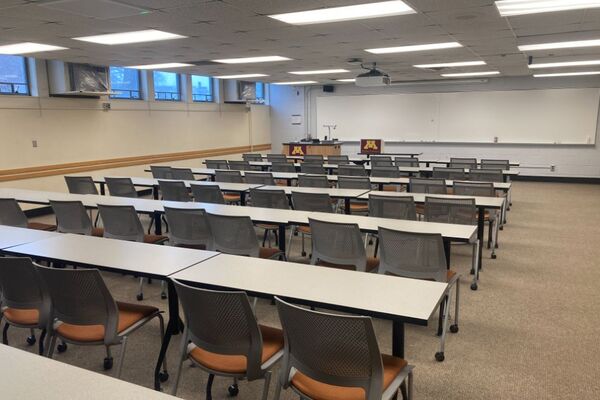 Back of room view of student table and chair seating and exit door at left rear of room