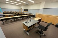 Back of room view of student tiered table and chair seating and display monitor on right rear wall