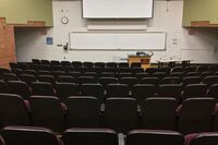 Front of room view with lectern center in front of markerboard and projection screen lowered