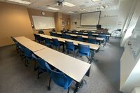 Front of room view with lectern on right in front of markerboard and projection screen lowered