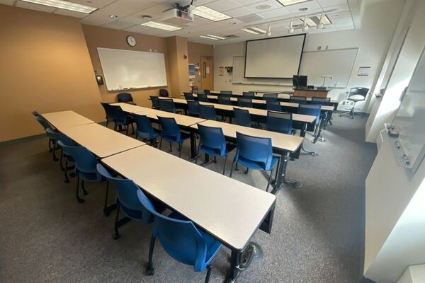 Front of room view with lectern on right in front of markerboard and projection screen lowered